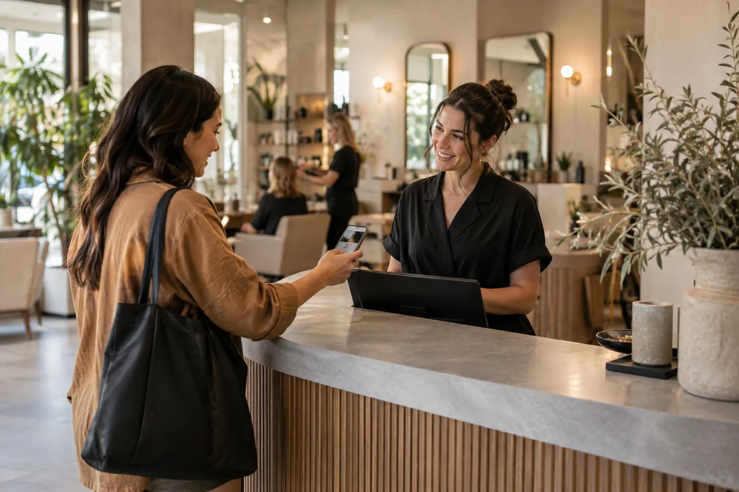A customer presenting a phone at a salon arrival desk as a receptionist welcomes them, candid wide photograph