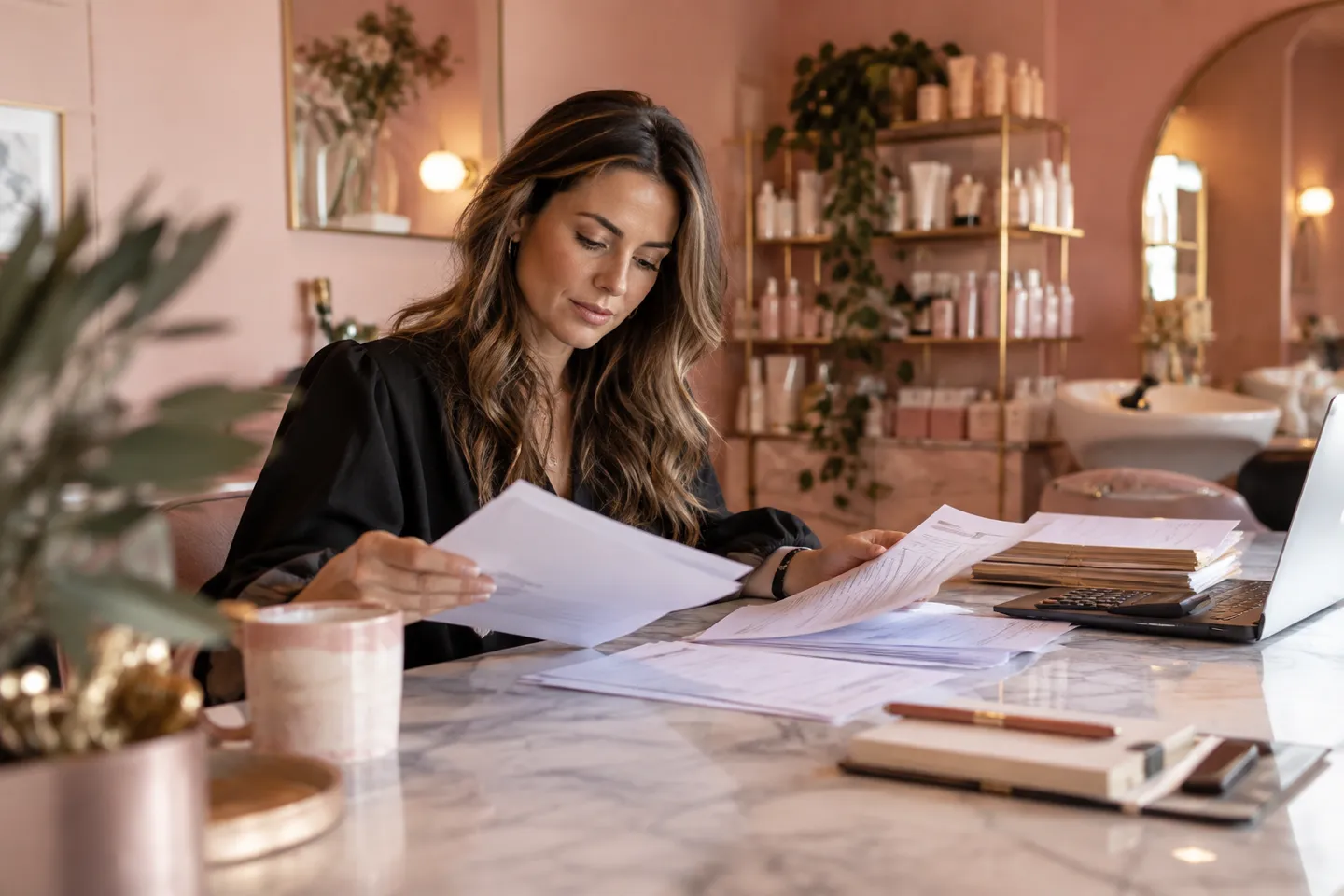 A beauty salon owner examining a stack of subscription invoices in a rose-colored office