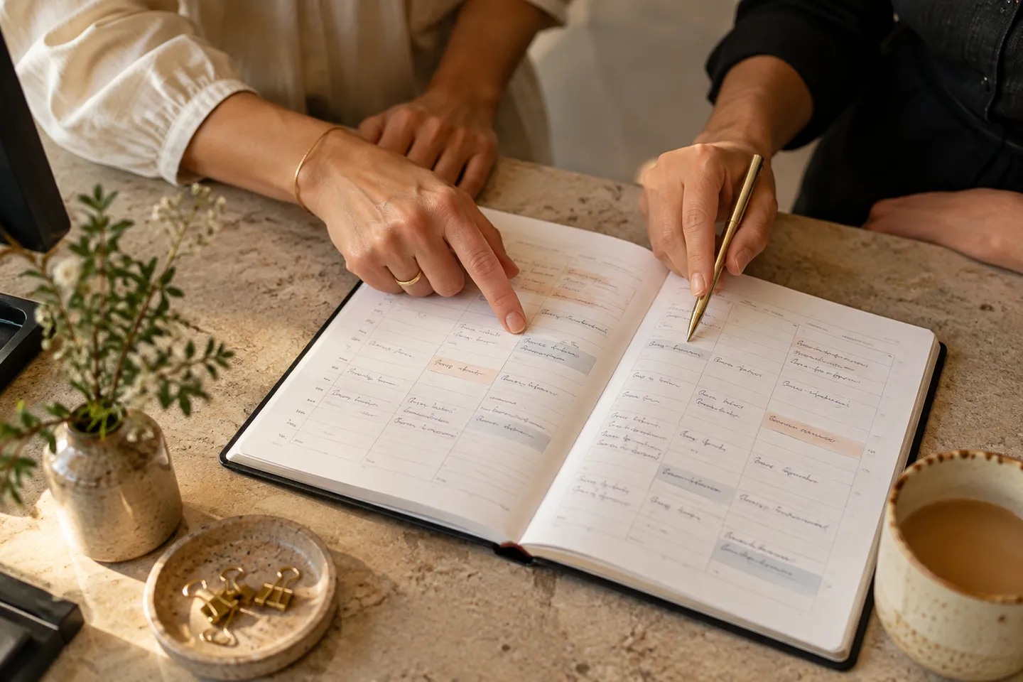 Two people pointing at an open appointment diary with unreadable handwriting, close-up from above