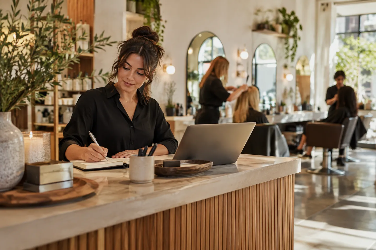A salon receptionist managing her desk while stylists work softly blurred in the background